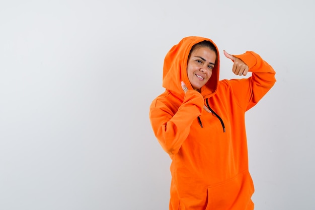 Female showing double thumbs up in orange hoodie and looking happy