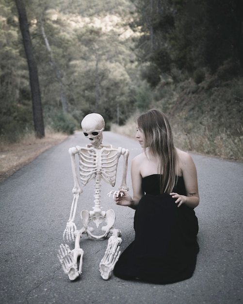 Free Photo female sitting on road and looking at artificial skeleton of man