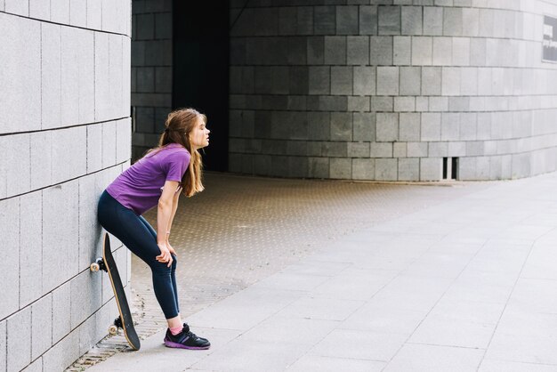 Female skateboarder rests against brick wall