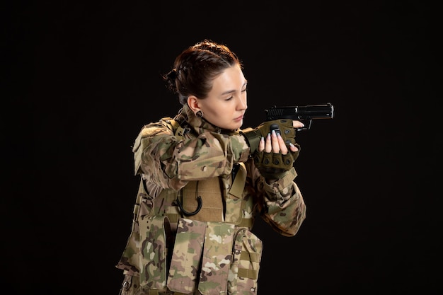 Free photo female soldier in camouflage aiming gun on black wall