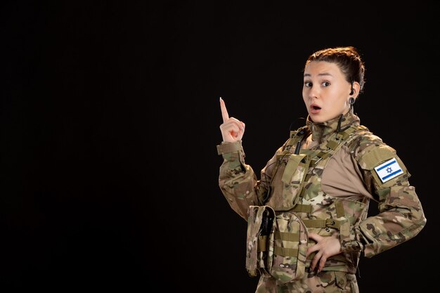 Female soldier in camouflage on a black wall