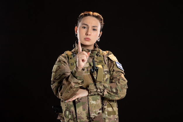 Free photo female soldier in camouflage warns on black wall