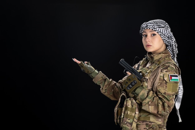 Free photo female soldier in military uniform with gun on black wall