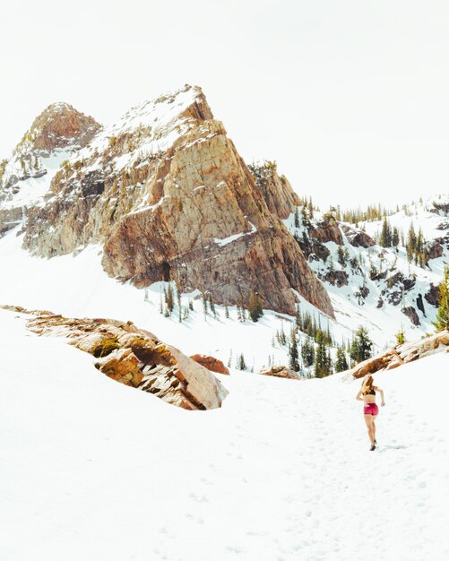 Female in sports outfit running in the snowy fields with high rocky mountains