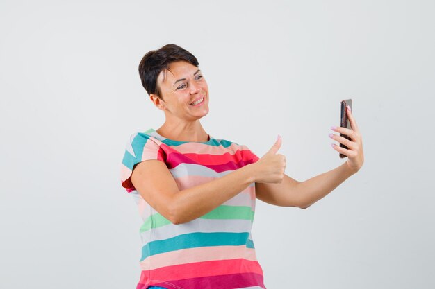 Female in striped t-shirt showing thumb up on video chat and looking cheerful , front view.