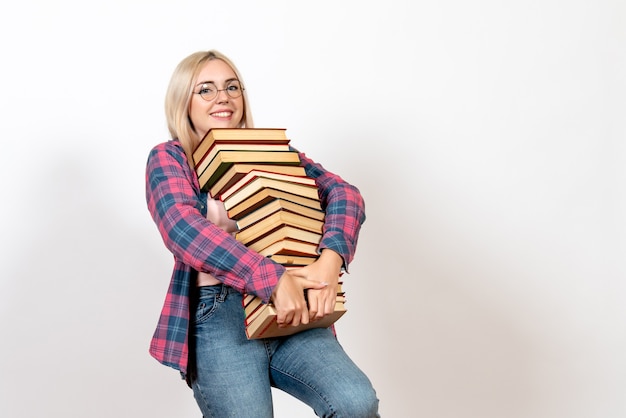 Free Photo female student holding different heavy books and smiling on white