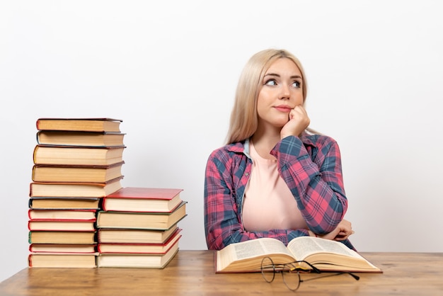 Free photo female student sitting with books and posing thinking on white