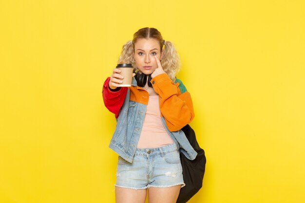 female student young in modern clothes holding coffee and posing on yellow