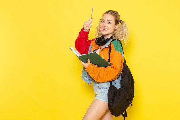 female student young in modern clothes holding copybook with smile on yellow