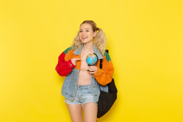 female student young in modern clothes holding a globe with smile on yellow