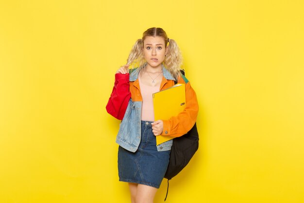 female student young in modern clothes holding yellow files just posing on yellow