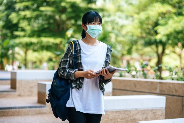 Female students wear masks, stand on stairs and hold books.