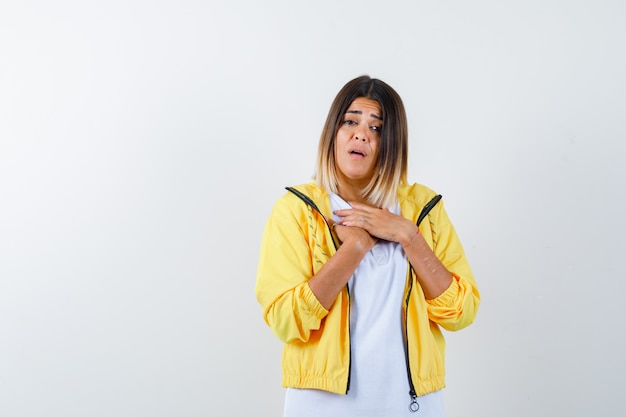 Female in t-shirt, jacket keeping hands on chest and looking puzzled , front view.