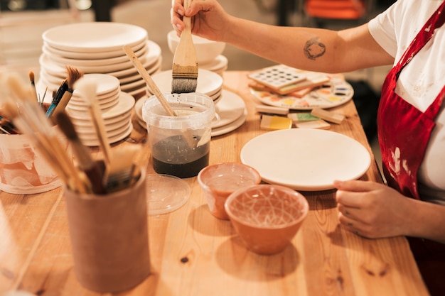 Female taking the ceramic color to paint on plate with brush