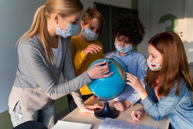 Free photo female teacher with medical mask teaching geography with earth globe in class