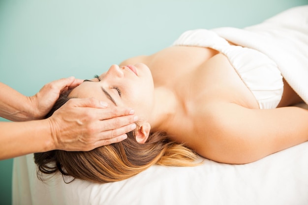 Female therapist balancing energy from a client during a reiki session at a health spa. Both hands on temple