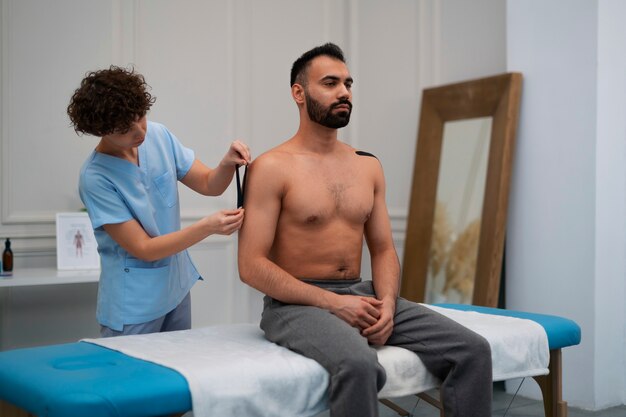 Female therapist in the rehabilitation center putting shoulder support on man