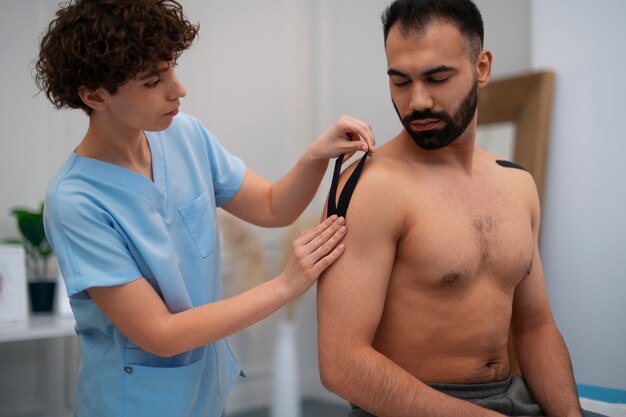 Female therapist in the rehabilitation center putting shoulder support on man