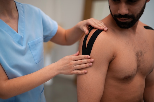 Female therapist in the rehabilitation center putting shoulder support on man