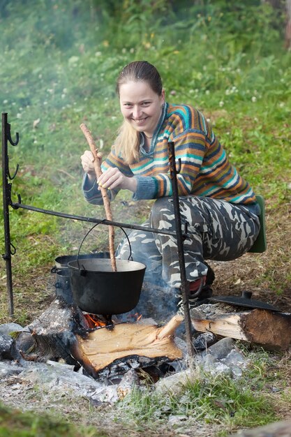 Female tourist cooking  food in cauldron