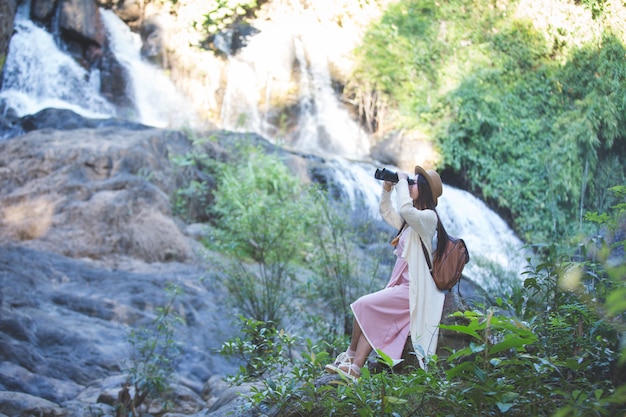 Free Photo female tourist who is looking at the binoculars to see the atmosphere at the waterfall