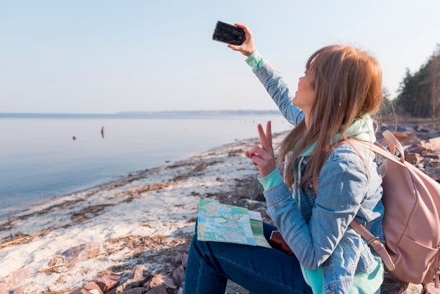 Free Photo female traveler sitting on beach taking selfie on mobile phone