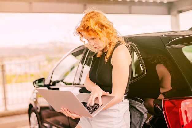 Female traveller with laptop standing beside car