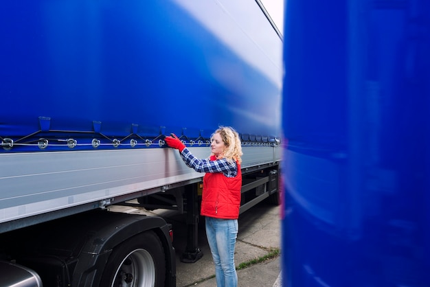 Free photo female truck driver checking vehicle and tightening truck tarpaulin