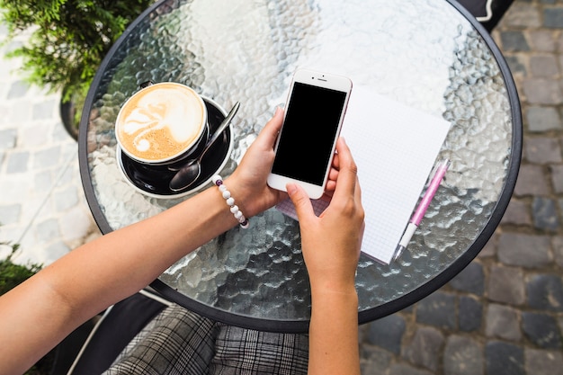 Female using cellphone with coffee cup over the glass table