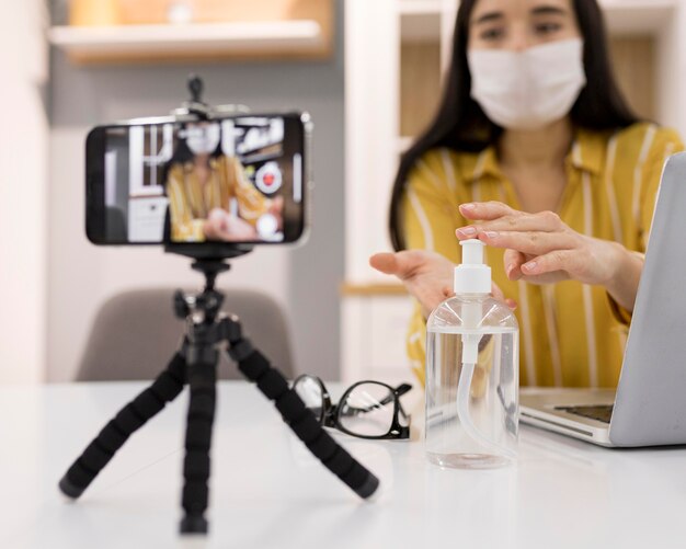 Female vlogger at home with smartphone and hand sanitizer