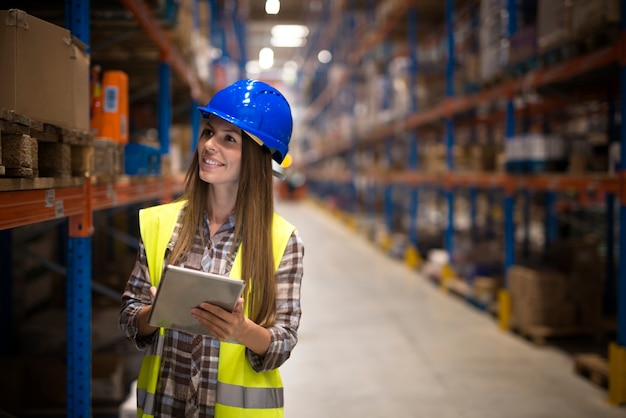 Female warehouse worker with tablet counting products on shelves in large storage area