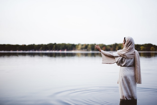 Female wearing a biblical robe and standing in the water with her hand up