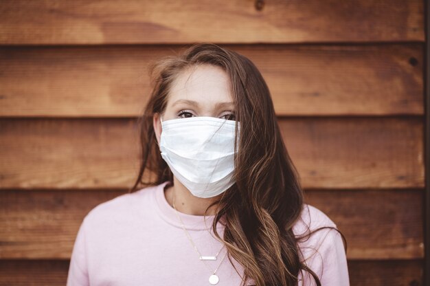 Female wearing a sanitary face mask in front of a wooden wall