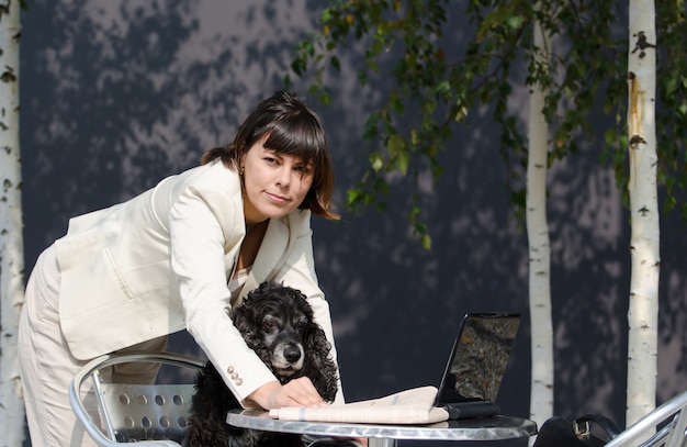 Free Photo female wearing a white suit holding her dog and using her laptop on the table