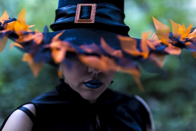 Female wearing a witch makeup and costume with a decorated hat captured in a forest