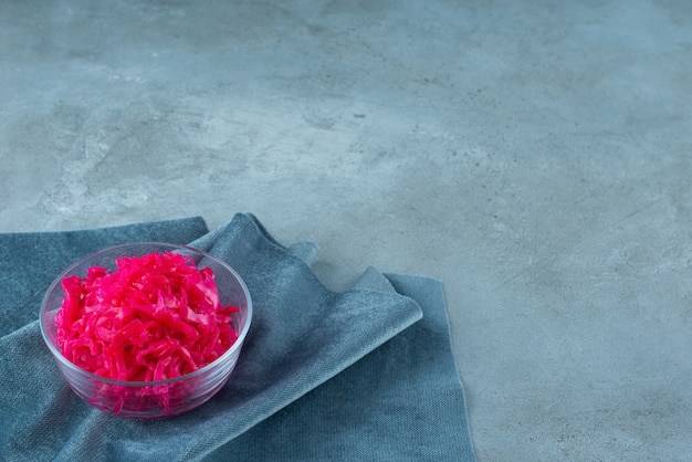 Fermented red cabbage lies in a bowl on piece of fabric, on the blue table. 