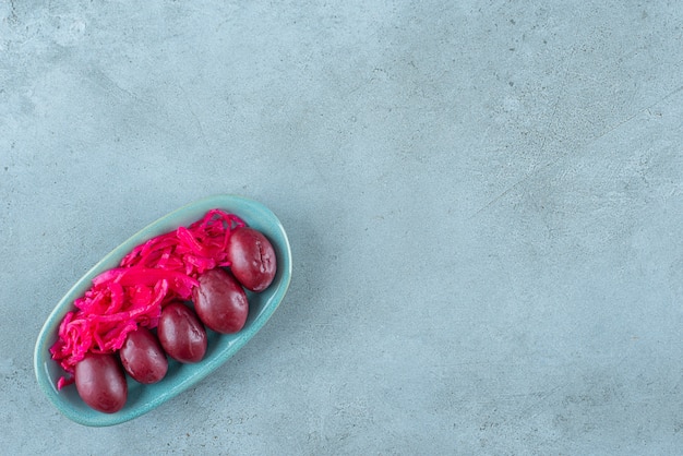 Fermented red sauerkraut with plums on a plate , on the blue table. 