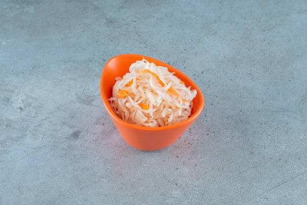 Free photo fermented sauerkraut with carrots in a plastic bowl on the blue surface