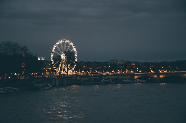 Free photo ferris wheel surrounded by a river and buildings under a cloudy sky during the night in paris