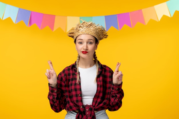 Festa junina blonde cute girl in straw hat brazilian festival with colorful flags crossing fingers