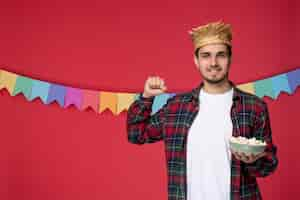 Free photo festa junina happy cute guy wearing straw hat celebrating brazilian festival eating popcorn