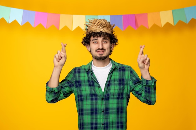 Free Photo festa junina young cute guy in straw hat and colorful flags brazilian festival fingers crossed