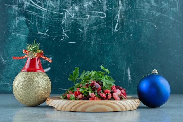 Festive baubles next to a platter of parsley topped vinegret salad on marble.