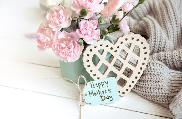 A festive composition with fresh flowers in a vase, decorative elements and a wish for a happy mother's day on a postcard.