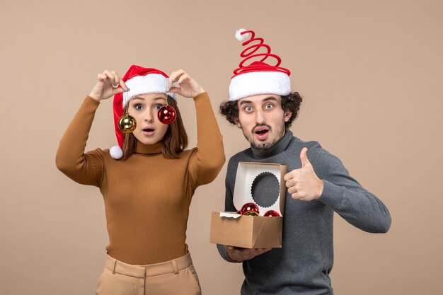 Festive mood with excited lovely couple wearing red santa claus hats on gray