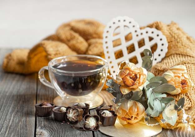 Festive still life for valentine's day with a drink in a cup, chocolates and flowers on a blurred background.