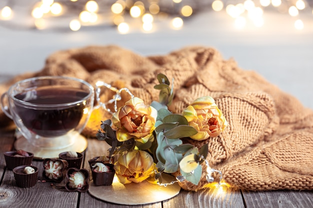 Festive still life with a drink in a cup, chocolates and flowers on a blurred table with bokeh.