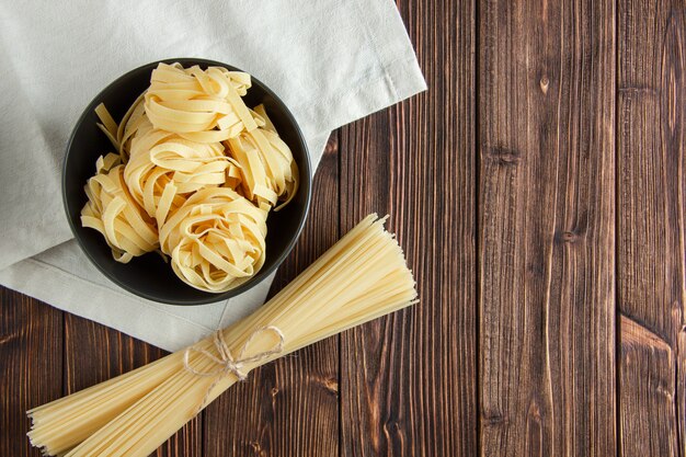 Fettuccine pasta with spaghetti in a bowl on wooden and kitchen towel background, flat lay.