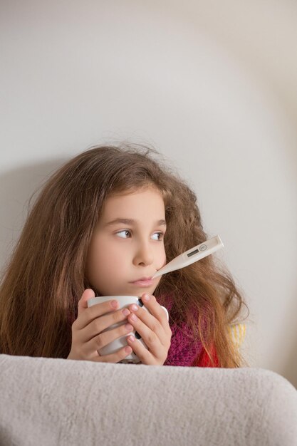 Fever cold and flu concepts Portrait of sad girl measuring temperature of body and holding cup of tea infront of her at home