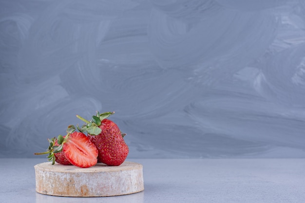 Free photo few strawberries on a piece of wood on marble background.